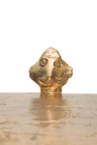 Gros plan sur la tête souriante qui sort du plateau du guéridon Him , en bronze doré d'Elizabeth Garouste