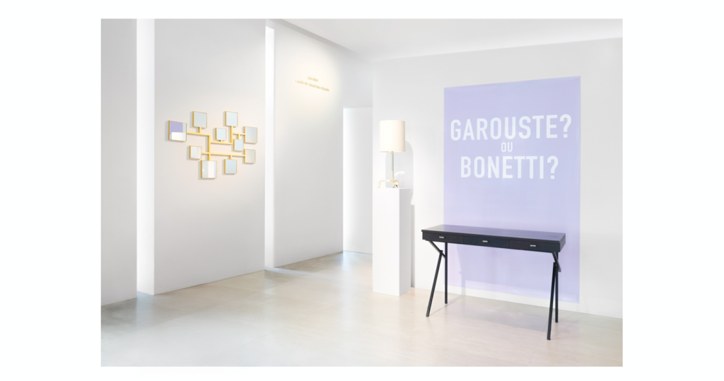 Septembre 2026, entrée de l'exposition "Garouste? ou Bonetti? "chez Sotrheby's Bureau en bois fonçé et pieds en forme d'équerre en fer forgé noir, Garouste et Bonetti, miroir constitué de plsuieurs petits carrés en fer forgé doré Elizabeth Garouste, Lampe en fer forgé argent Mattia Bonetti